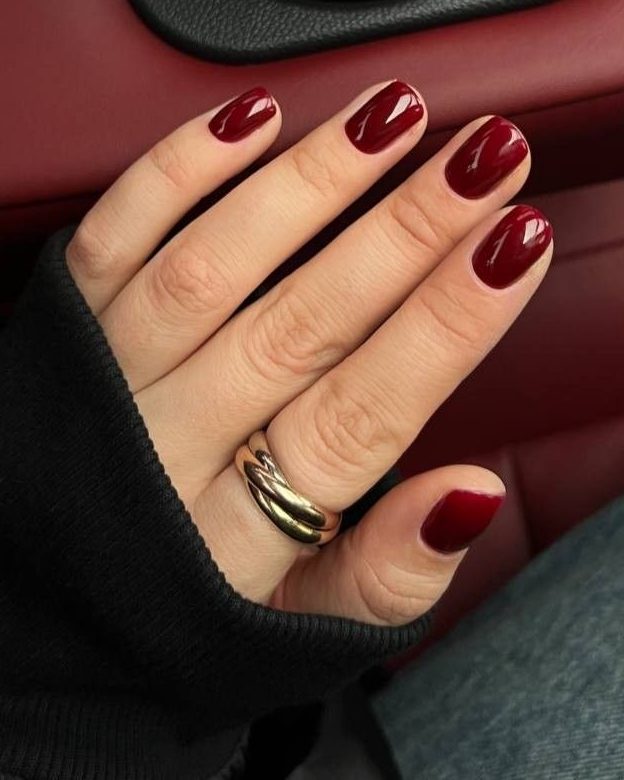 Short nails in glossy wine red, hand with a gold ring